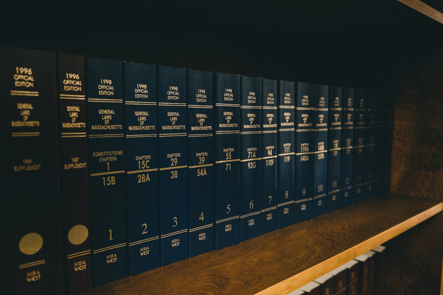 File di libri legali blu scuro con scritte dorate su uno scaffale.