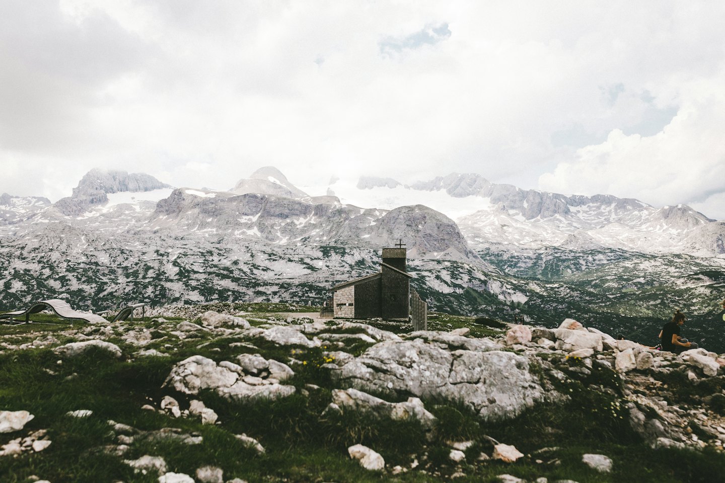 Moderna cappella in pietra immersa in un paesaggio montano alpino roccioso.