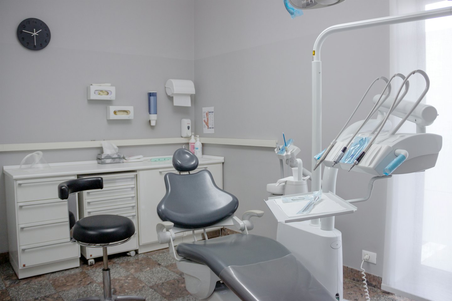 Moderna sala d'esame dentistico vuota con sedia grigia e attrezzature bianche.
