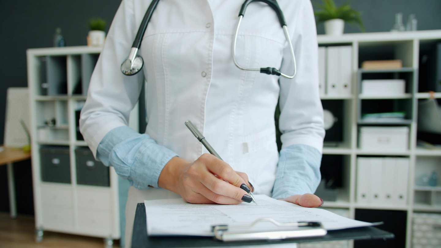 Medico che scrive appunti su una cartellina in un ufficio.