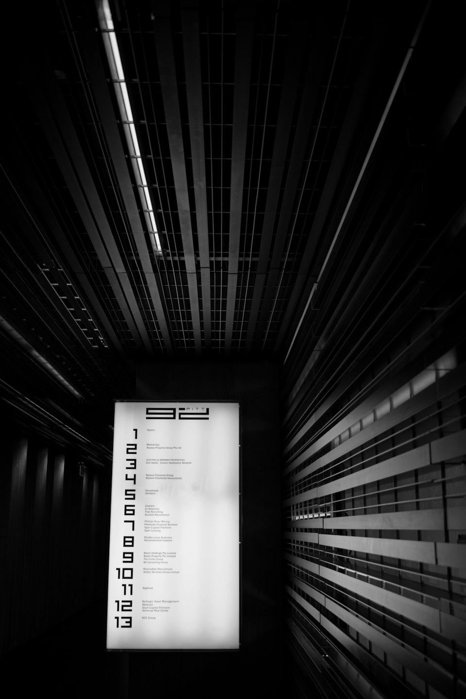 Un pannello informativo illuminato elenca i nomi delle attività in un corridoio moderno.