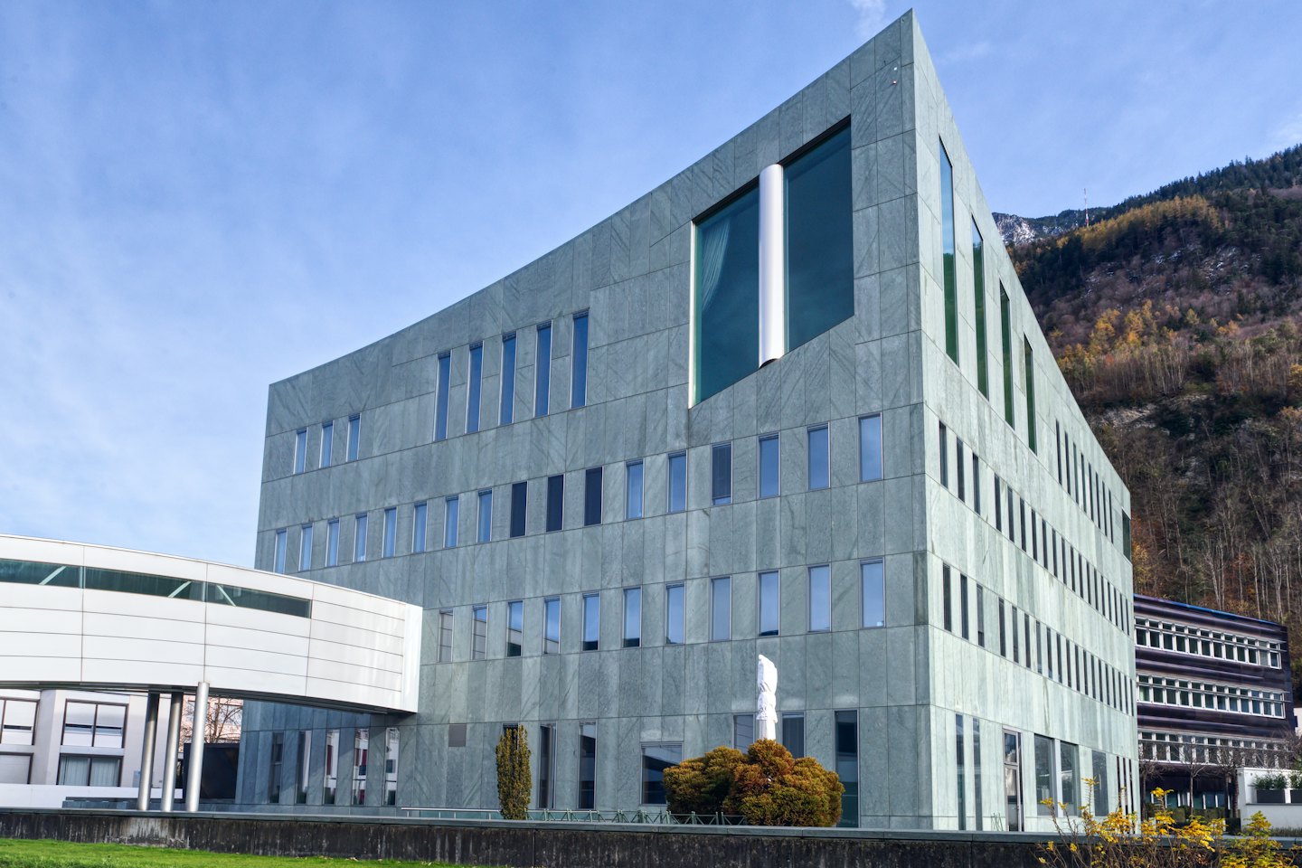 Moderno edificio per uffici in pietra davanti a una montagna con fogliame autunnale.