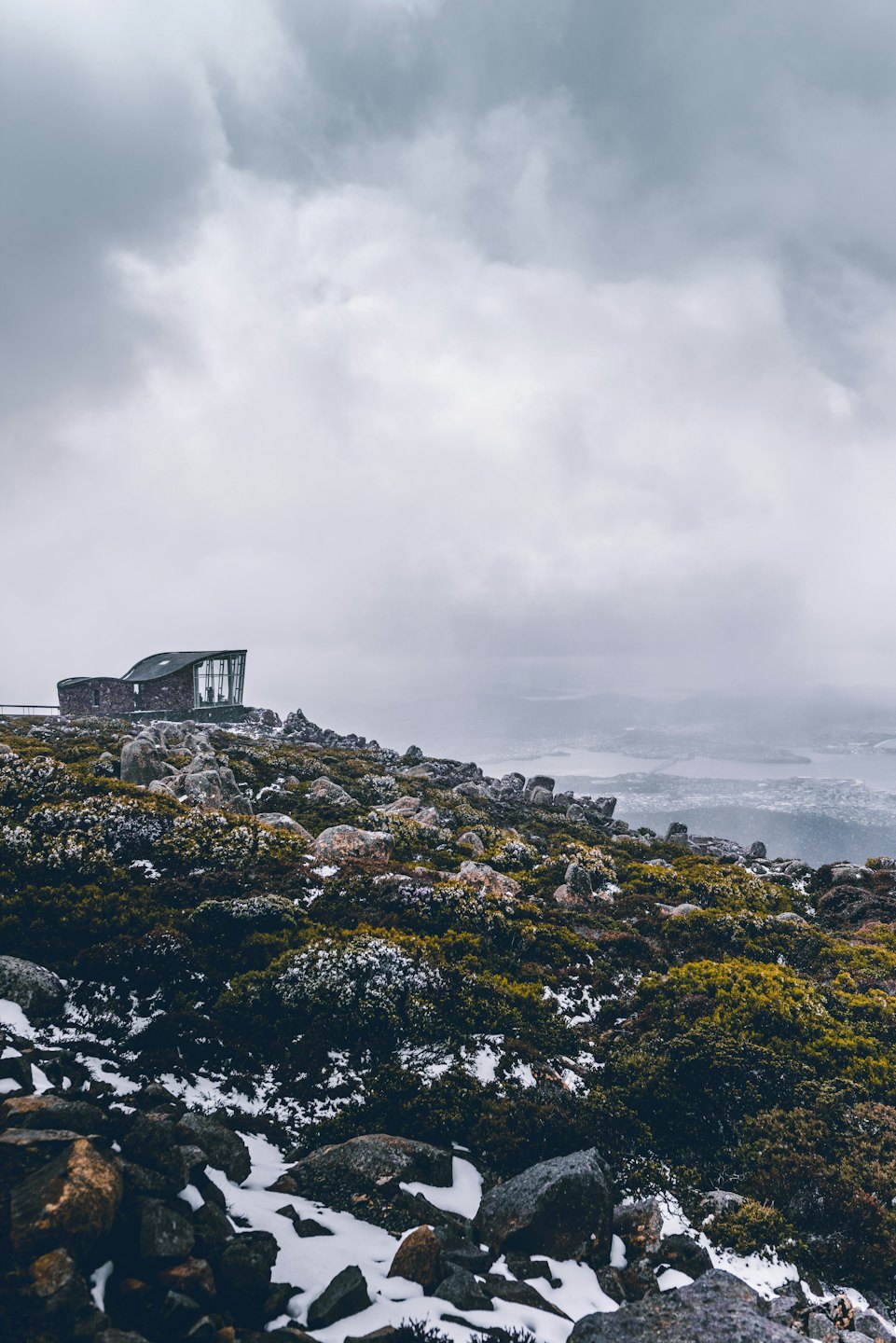 Moderno edificio in pietra e vetro su un picco montuoso innevato.