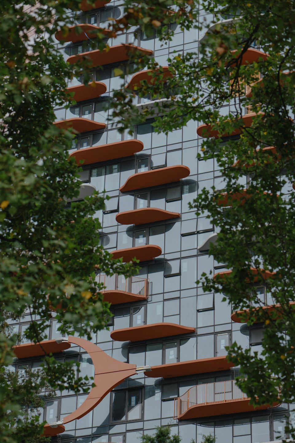 Facciata di un edificio moderno con balconi curvi e fogliame verde.