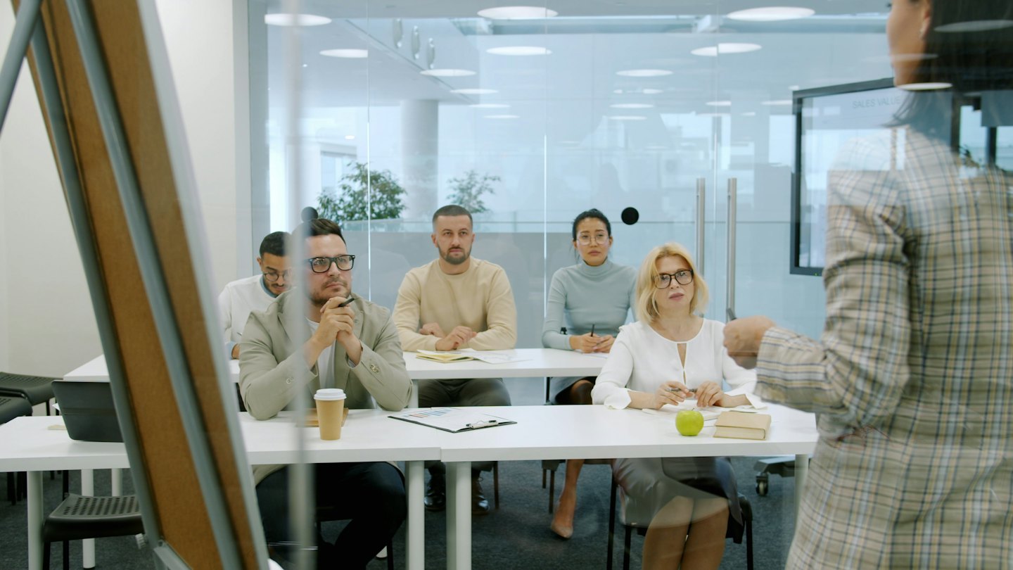 Professionisti diversi ascoltano un relatore in una moderna sala conferenze.