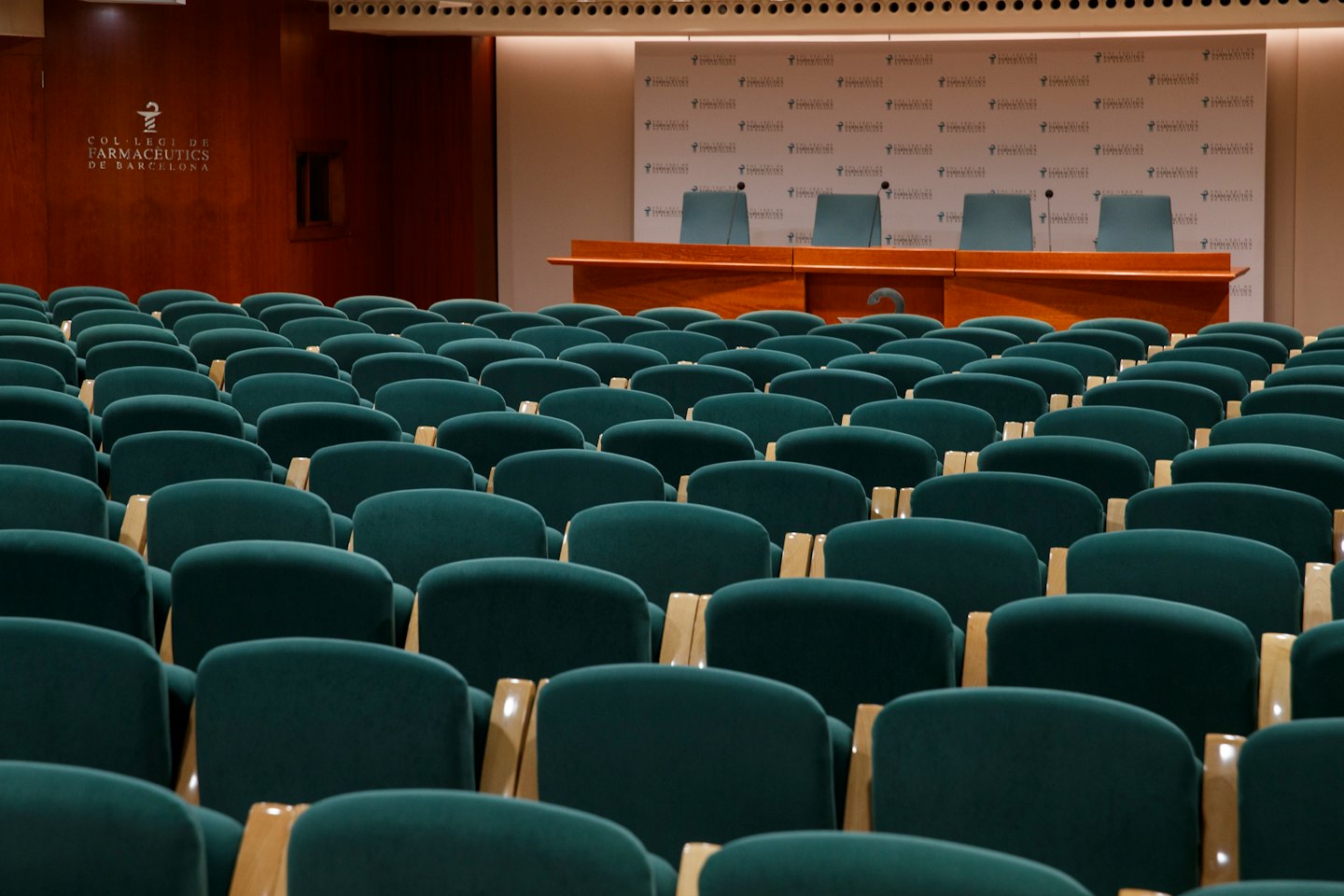 Sala conferenze vuota con sedie verdi e un palco.